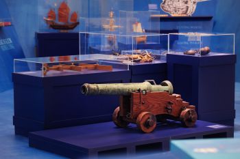 Kanone auf einem Podest, im Hintergrund mehrere Vitrinen mit Schiffsmodellen, Enterhaken, Jakobstab, Metallkugeln